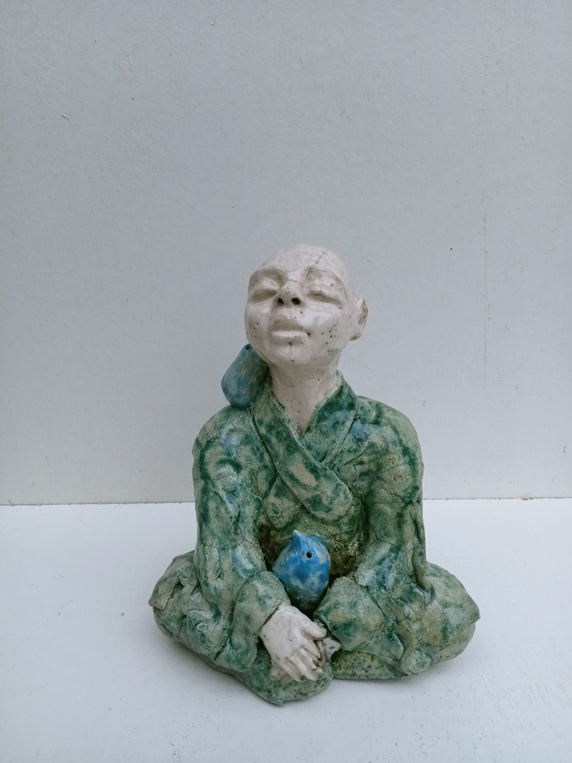 moine tibétain assis avec un oiseau bleu entre ses bras et un sur son épaule droite